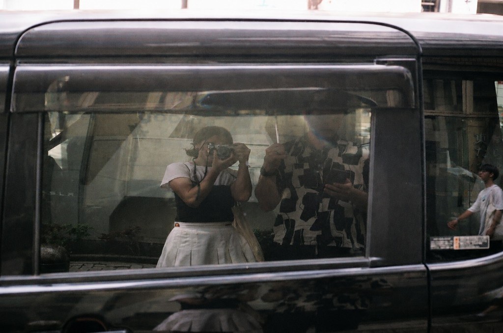 Reflection of Katherine in a car window on a city street